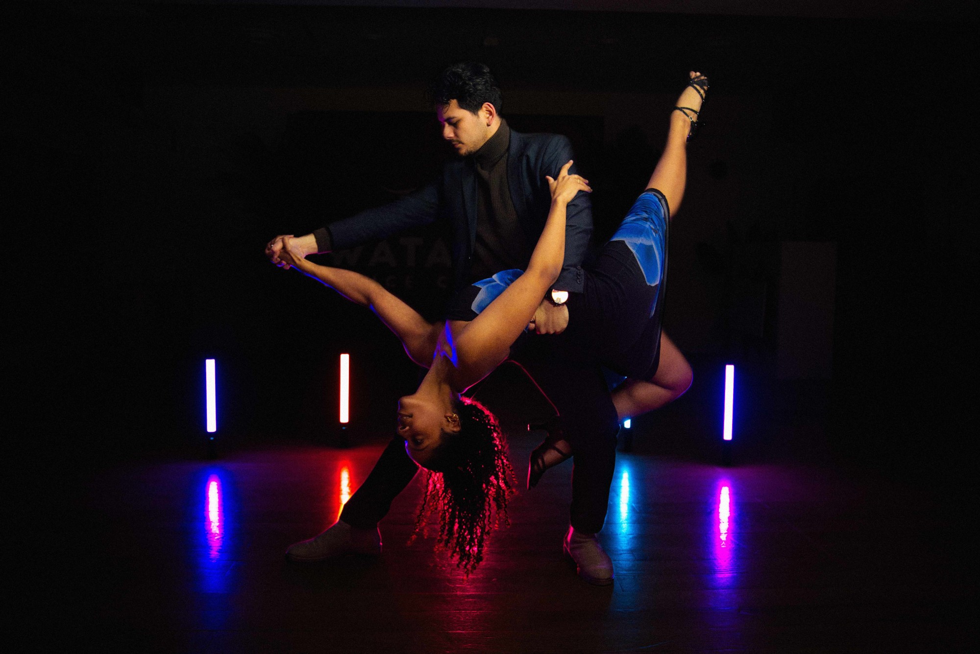 Watapana salsa dancers performing a dip in the studio with coloured lights
